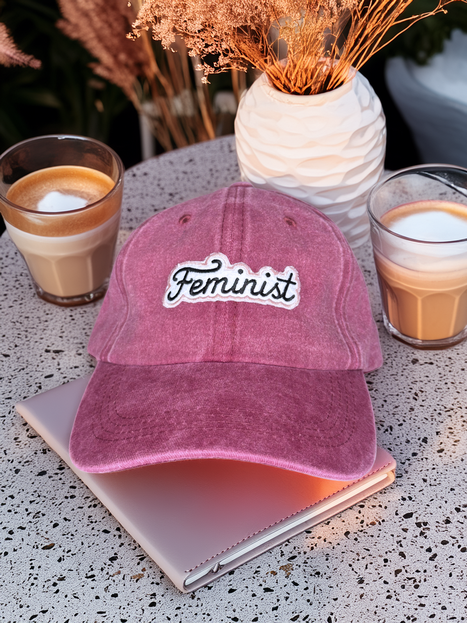 Pink 'Feminist' cap on a table with coffee and decor