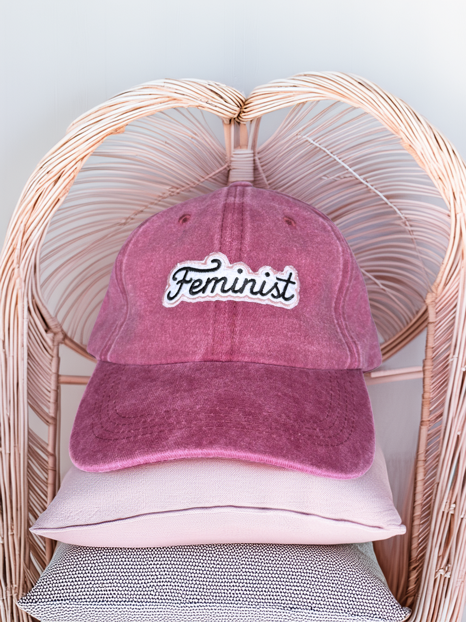 Pink 'Feminist' cap on a wicker chair with a light gray background