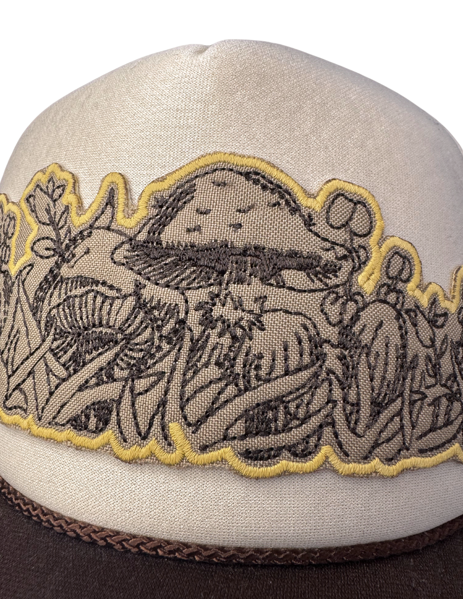 Closeup of detailed black mushroom embroidery with golden scalloped edge patch on foam-front trucker hat

