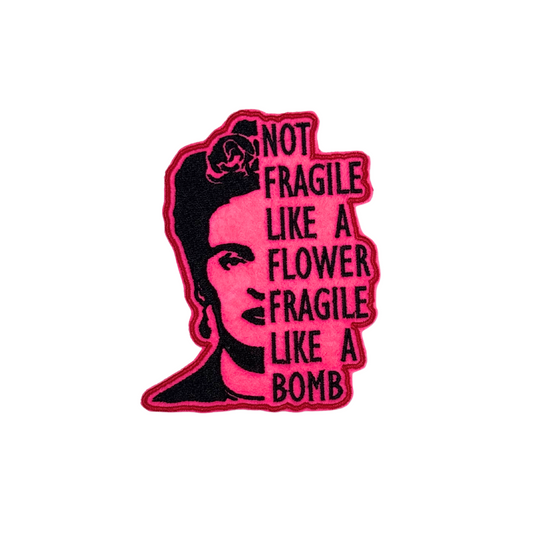 "Bright pink embroidered patch featuring a black portrait of Frida Kahlo with the phrase 'Not Fragile Like a Flower, Fragile Like a Bomb.'"
