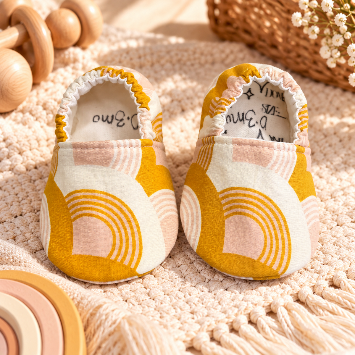 Golden Rainbow soft sole baby moccasins in mustard, cream and blush, size 0–3 months, styled in a warm boho nursery scene