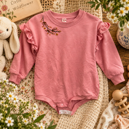 Hand-embroidered pink floral baby onesie styled with warm vintage nursery details
