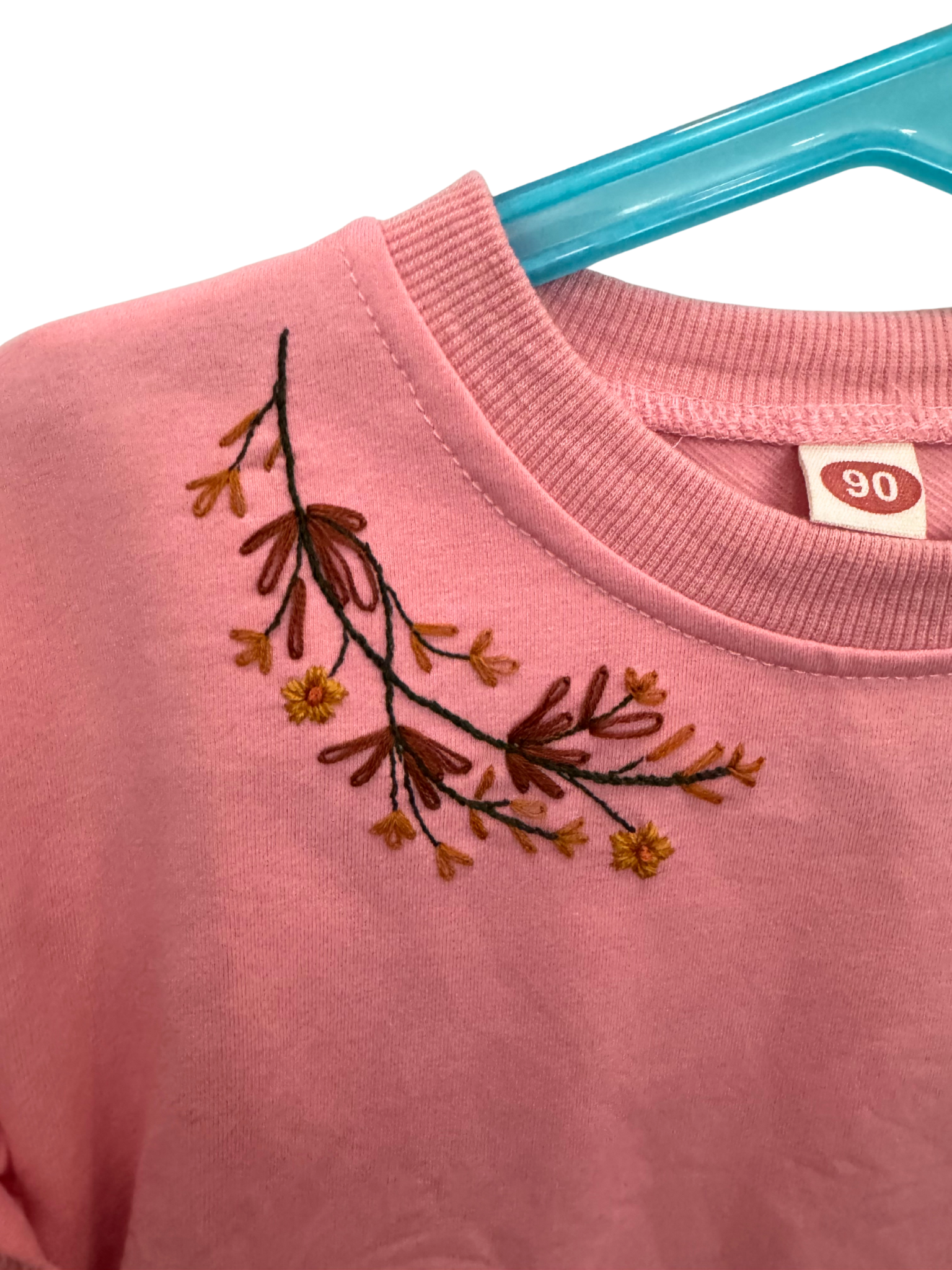 Pink sweatshirt with embroidered floral design on a hanger