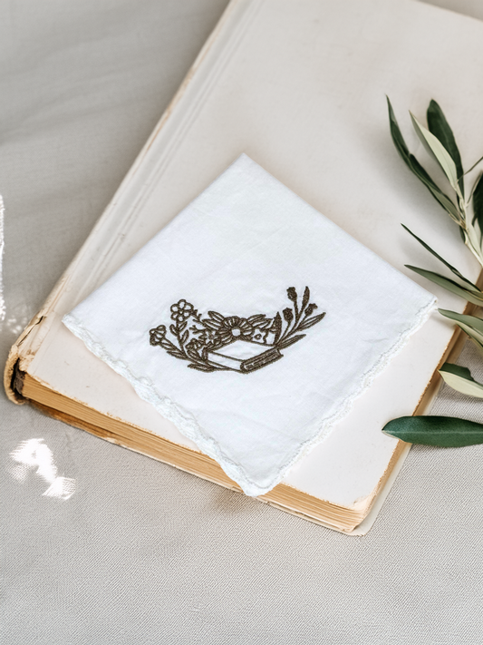 White embroidered handkerchief with olive book and floral design styled on a vintage book with greenery

