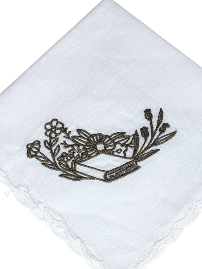 Close-up of olive thread embroidered open book with flowers on scalloped white cotton

