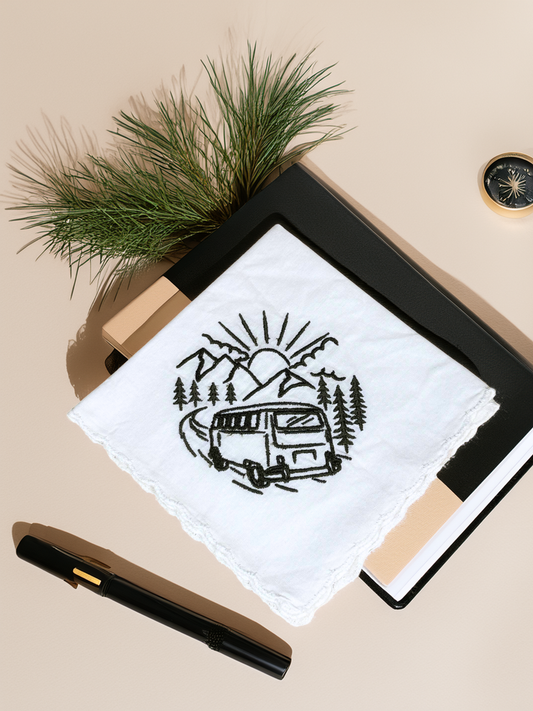 White handkerchief with black embroidered camper van and mountain scene, styled with pine sprigs and a journal