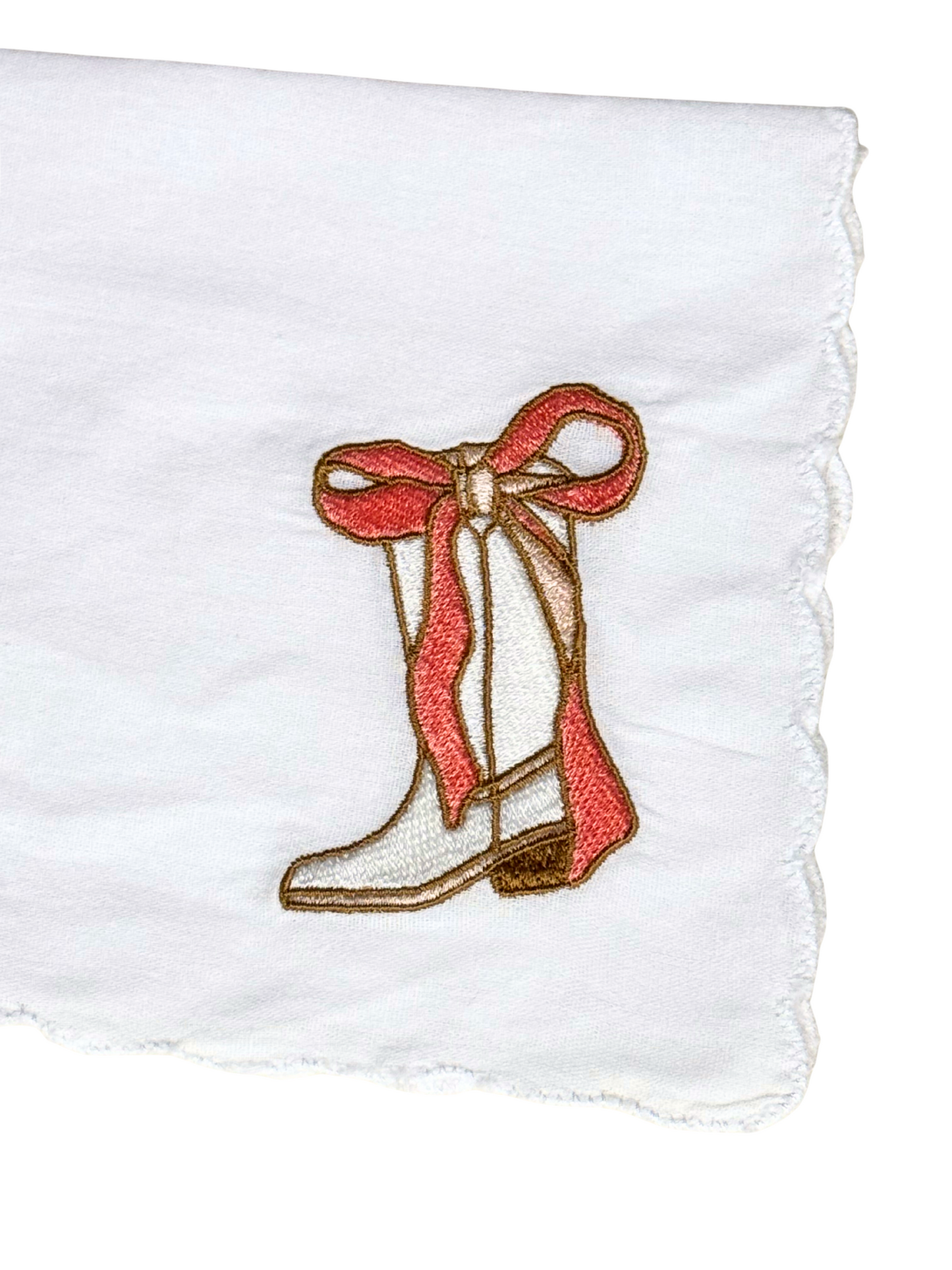 Close-up of cowgirl boot and bow embroidery on scalloped white handkerchief


