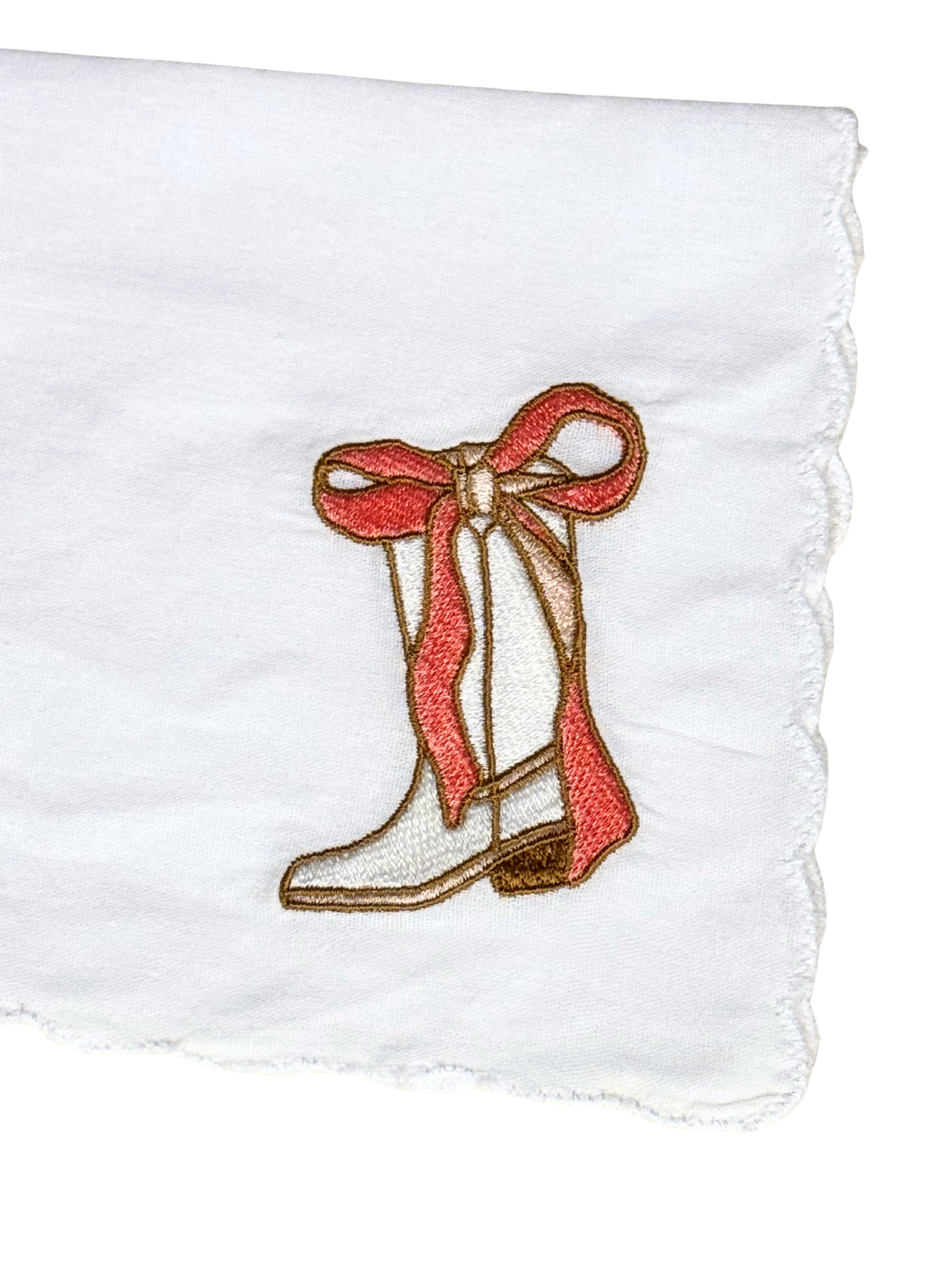 Close-up of cowgirl boot and bow embroidery on scalloped white handkerchief

