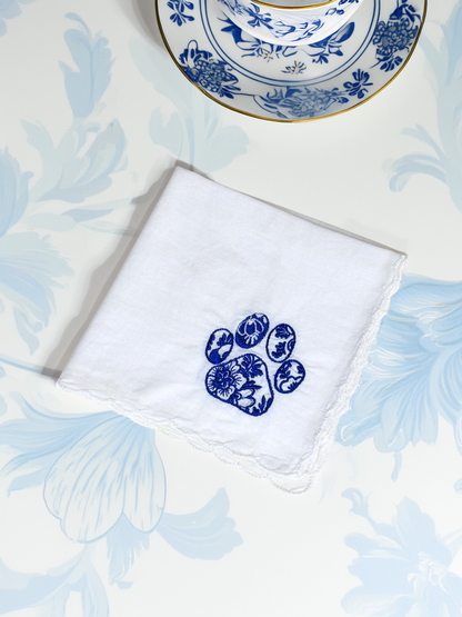 White embroidered handkerchief with blue floral dog paw, styled with chinoiserie teacup on matching floral background


