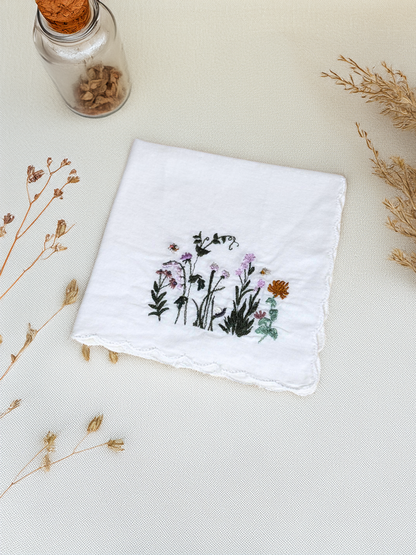 Closeup of white embroidered handkerchief featuring fairy garden wildflowers and bees

