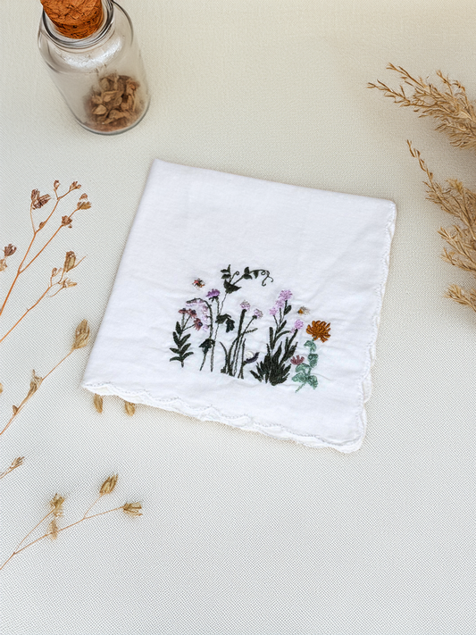 Closeup of white embroidered handkerchief featuring fairy garden wildflowers and bees


