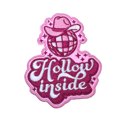 Close-up of a pink embroidered patch featuring a disco ball wearing a cowboy hat with the words "Hollow Inside" in cursive.
