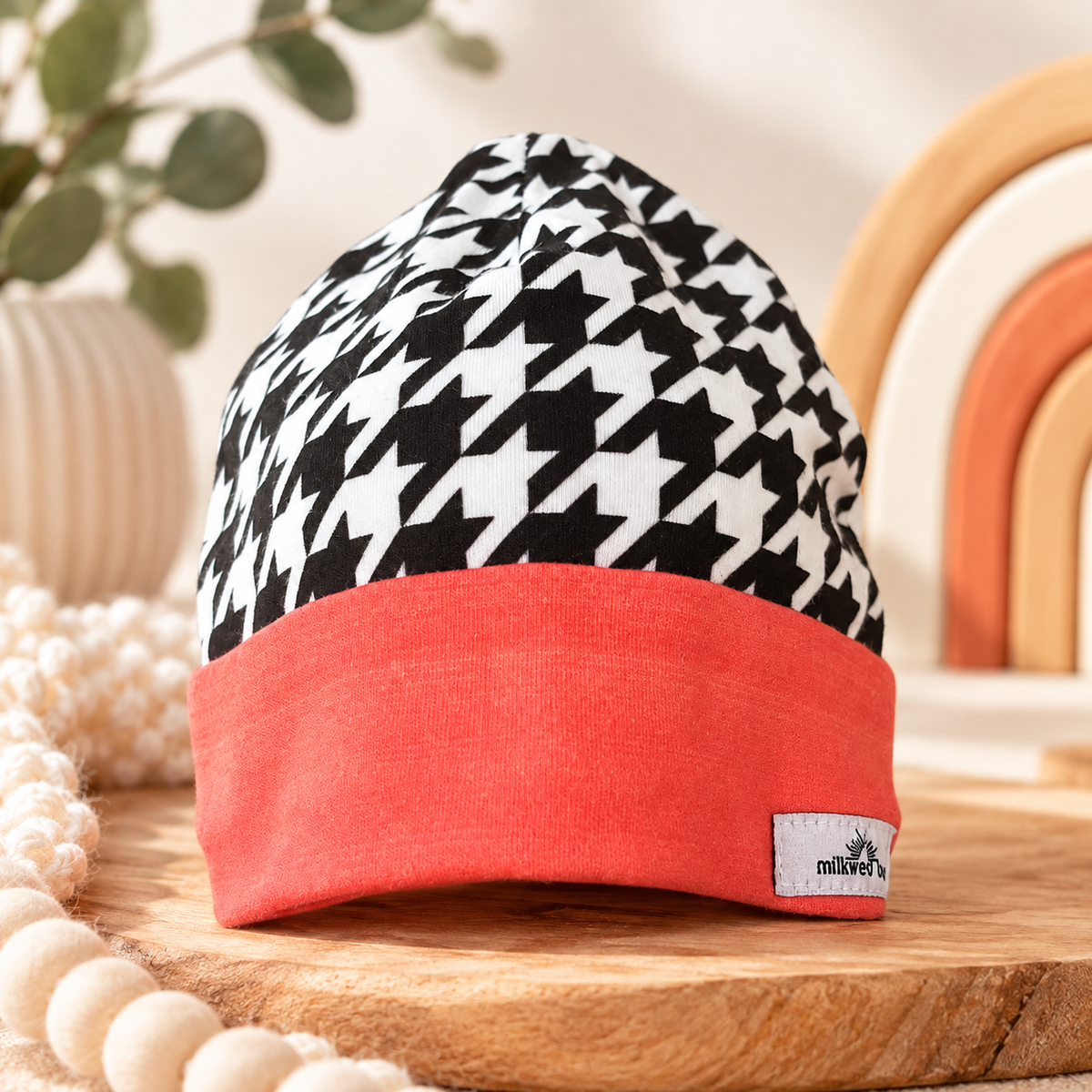 Black and white houndstooth baby beanie with coral cuff styled on warm wooden surface