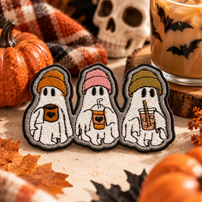Three embroidered coffee ghosts in knit beanies, photographed with Halloween pumpkins and autumn decorations