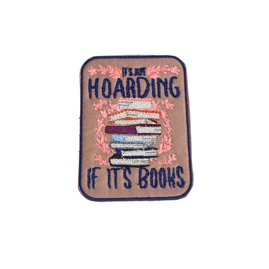 Embroidered patch featuring a stack of books with the phrase "It's Not Hoarding If It's Books," surrounded by floral detailing.
