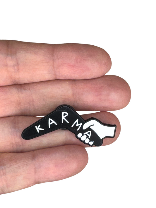 Karma enamel pin held between fingers to show size
