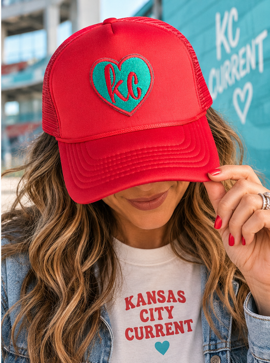 Model wearing red and teal KC Current heart trucker hat