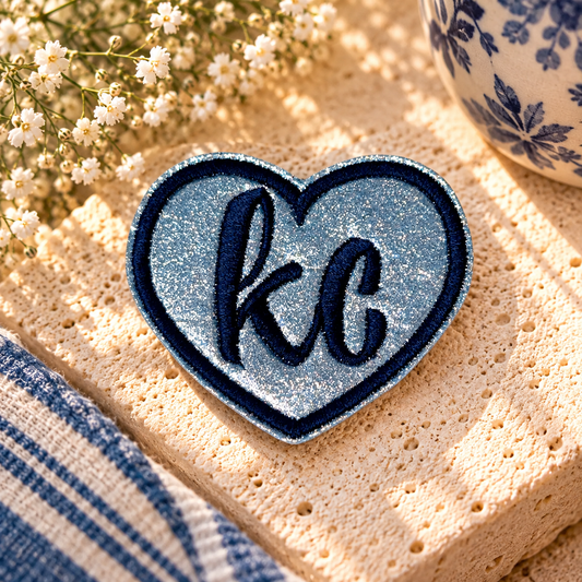 Silver glitter KC heart iron-on patch with navy embroidered letters and border, styled hero photo