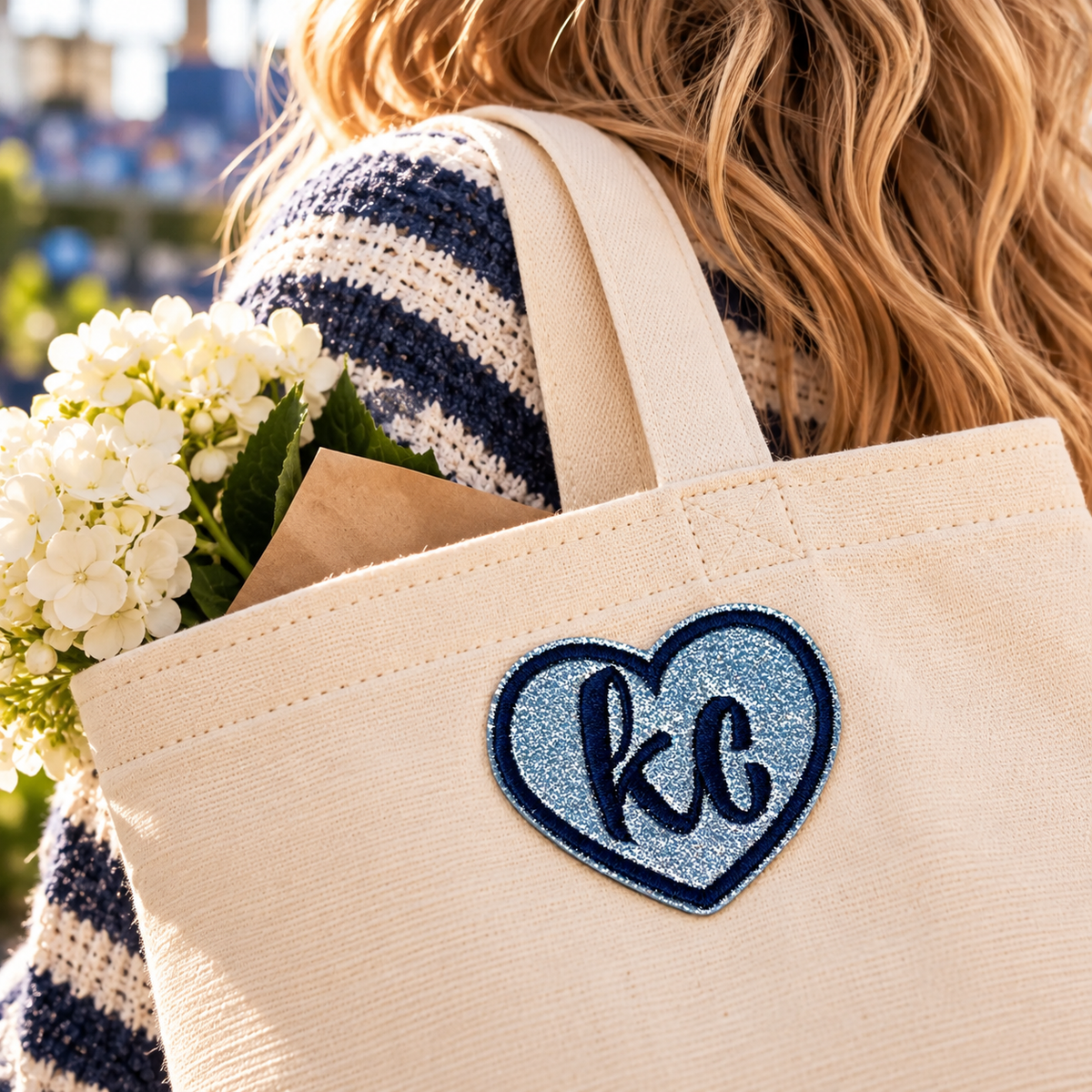 Silver glitter KC heart patch attached to a cream canvas tote, carried outdoors