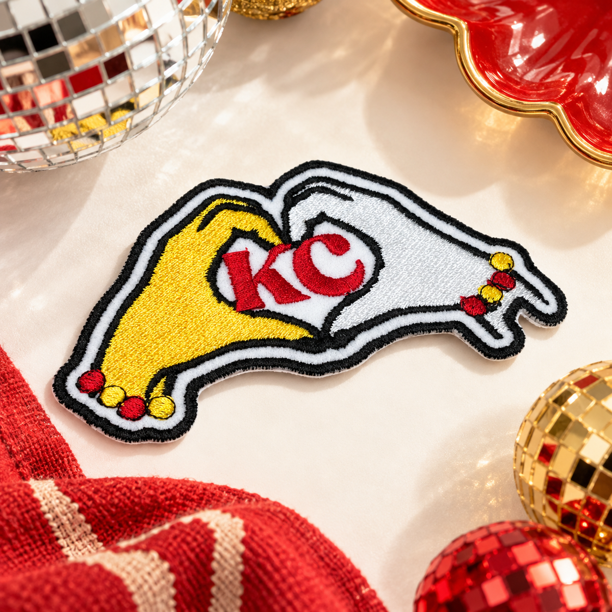 KC heart hands embroidered iron-on patch with yellow and white hands and red KC lettering, styled with red and gold accessories