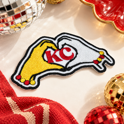 KC heart hands embroidered iron-on patch with yellow and white hands and red KC lettering, styled with red and gold accessories