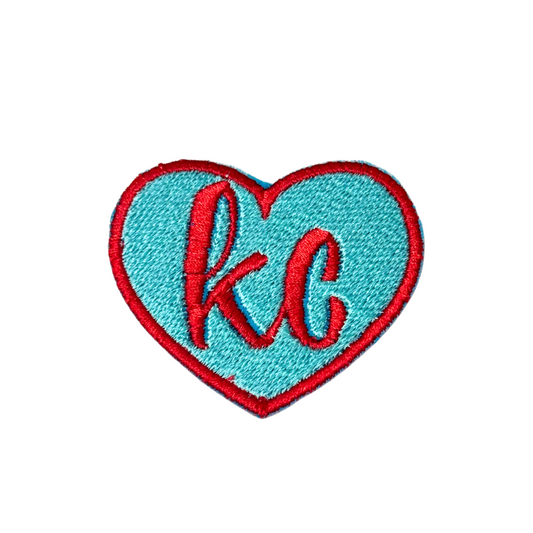 Embroidered aqua blue and red heart-shaped KC patch on white background

