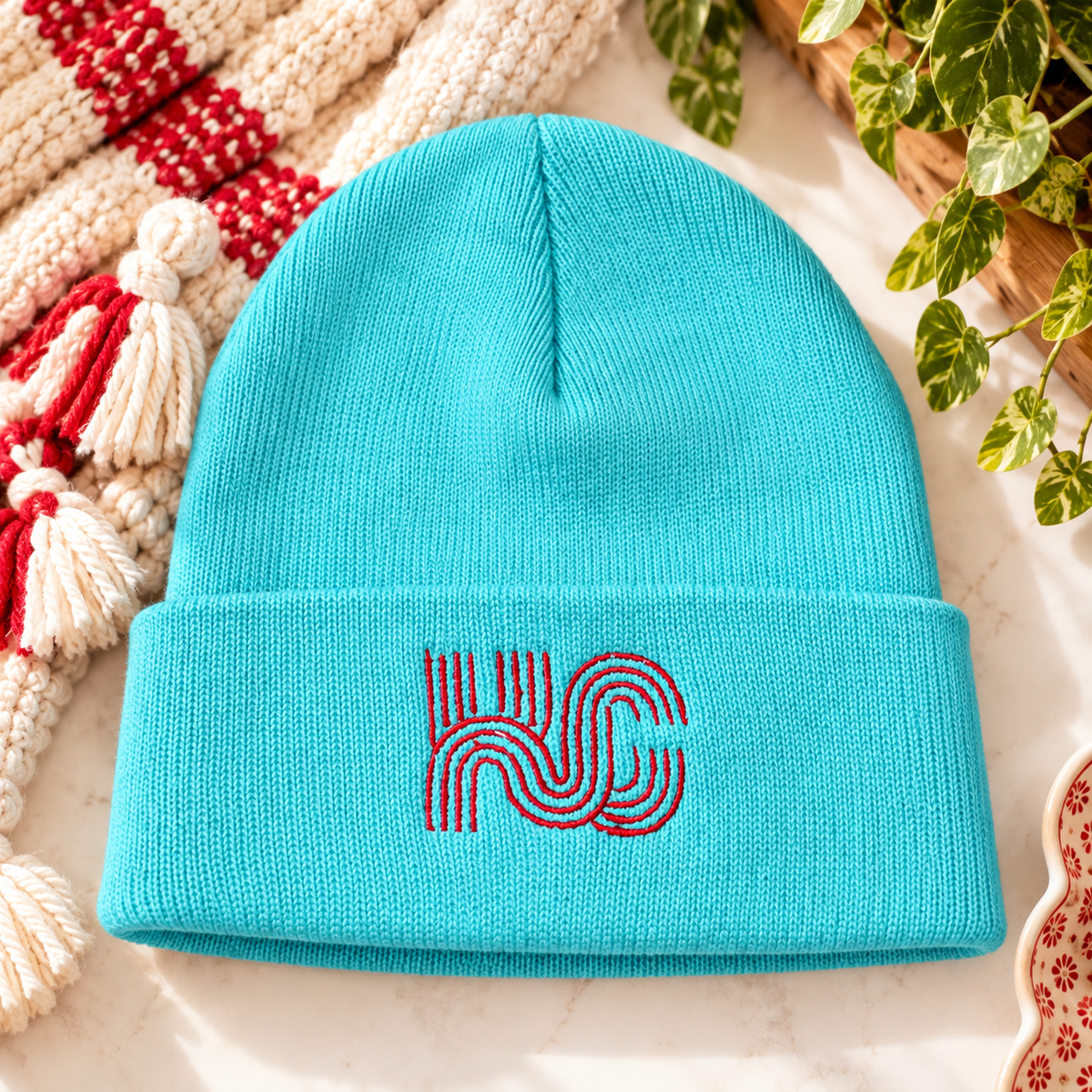 Teal knit beanie with red KC geometric embroidery on the folded cuff, styled with cream and red accents