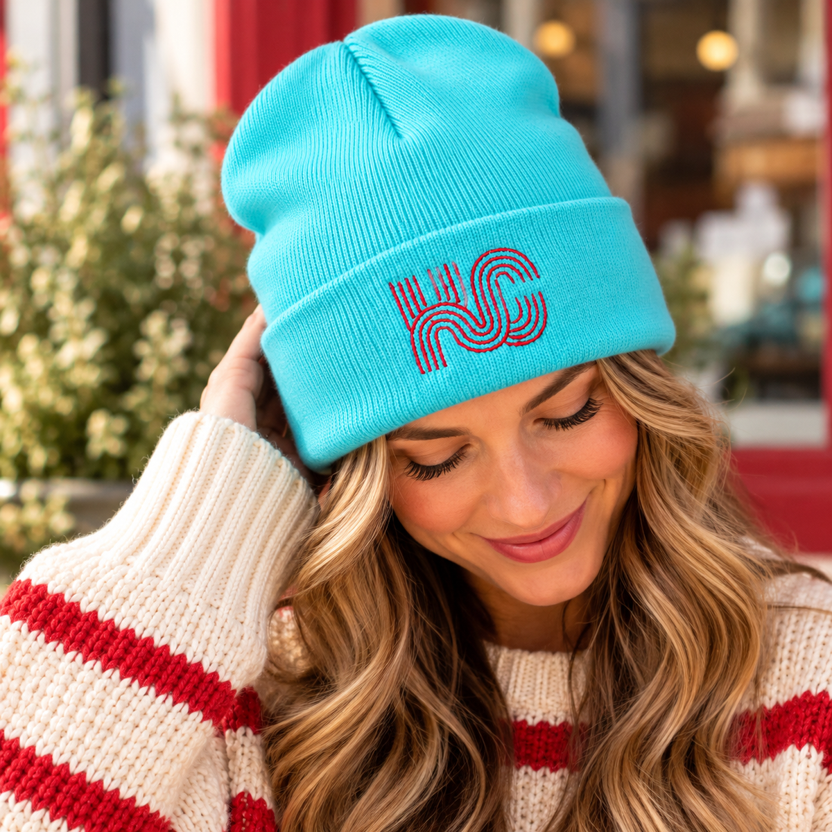 Adult wearing a teal knit KC beanie with red geometric embroidery on the folded cuff