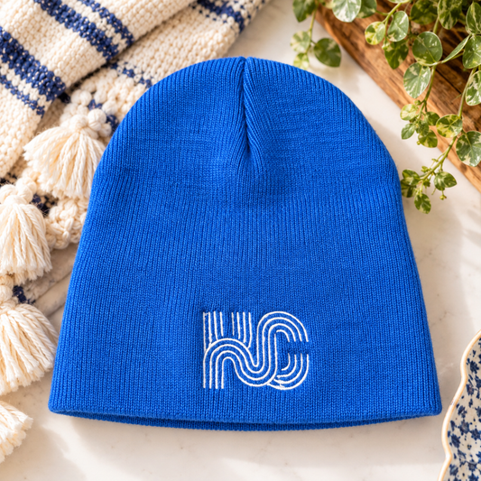 Royal blue KC embroidered beanie with white logo, styled on a cream surface with blue and ivory accents