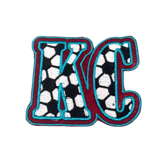 Front view of KC embroidered soccer patch with maroon and aqua outline
