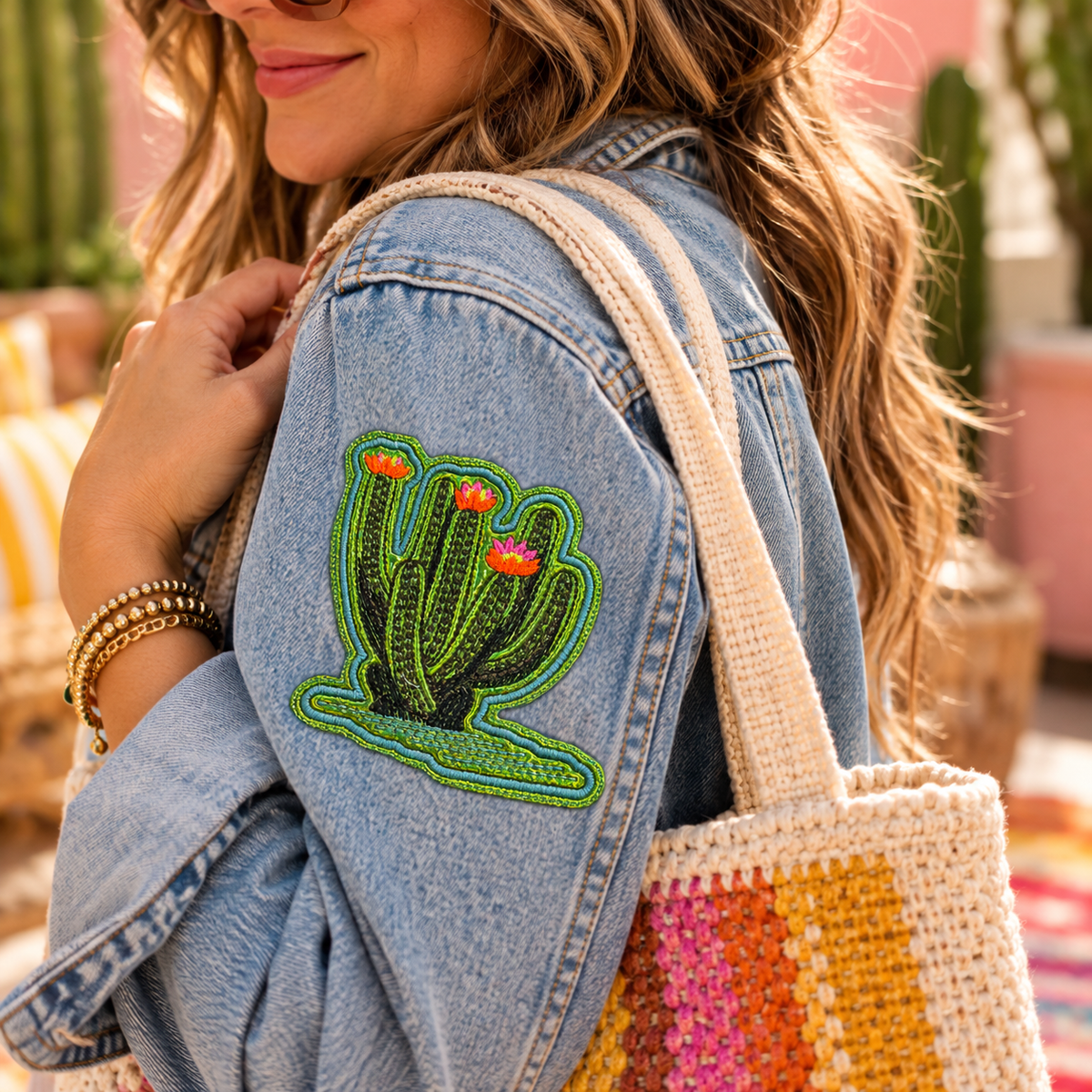 Large green flowering cactus embroidered iron-on patch displayed on the sleeve of a light blue denim jacket in a sunny outdoor scene
