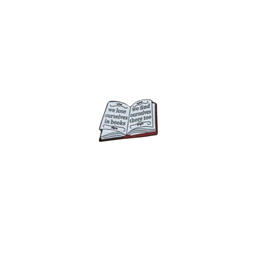 Enamel pin shaped like an open book with the quote “we lose ourselves in books, we find ourselves there too”

