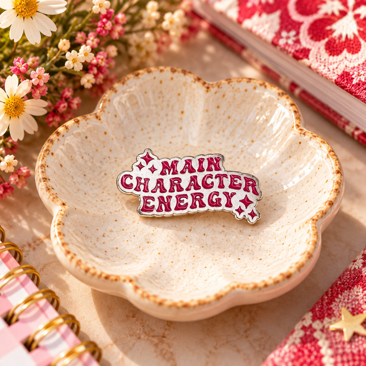 Main Character Energy red and silver enamel pin styled in a cream ceramic dish