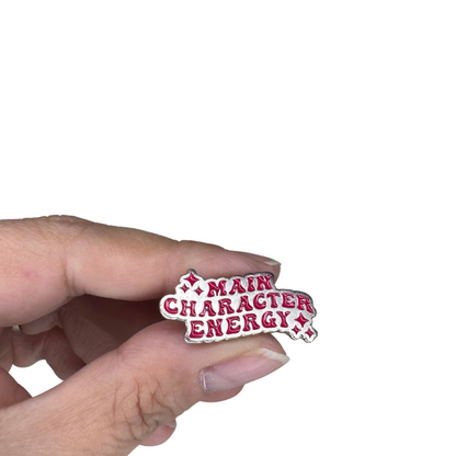 Close-up scale image of the "Main Character Energy" enamel pin held in hand
