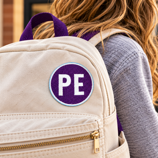 Purple and white Prairie Elementary PE embroidered patch attached to a cream backpack worn by a student