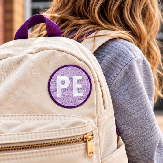 Lavender Prairie Elementary PE patch attached to a cream school backpack