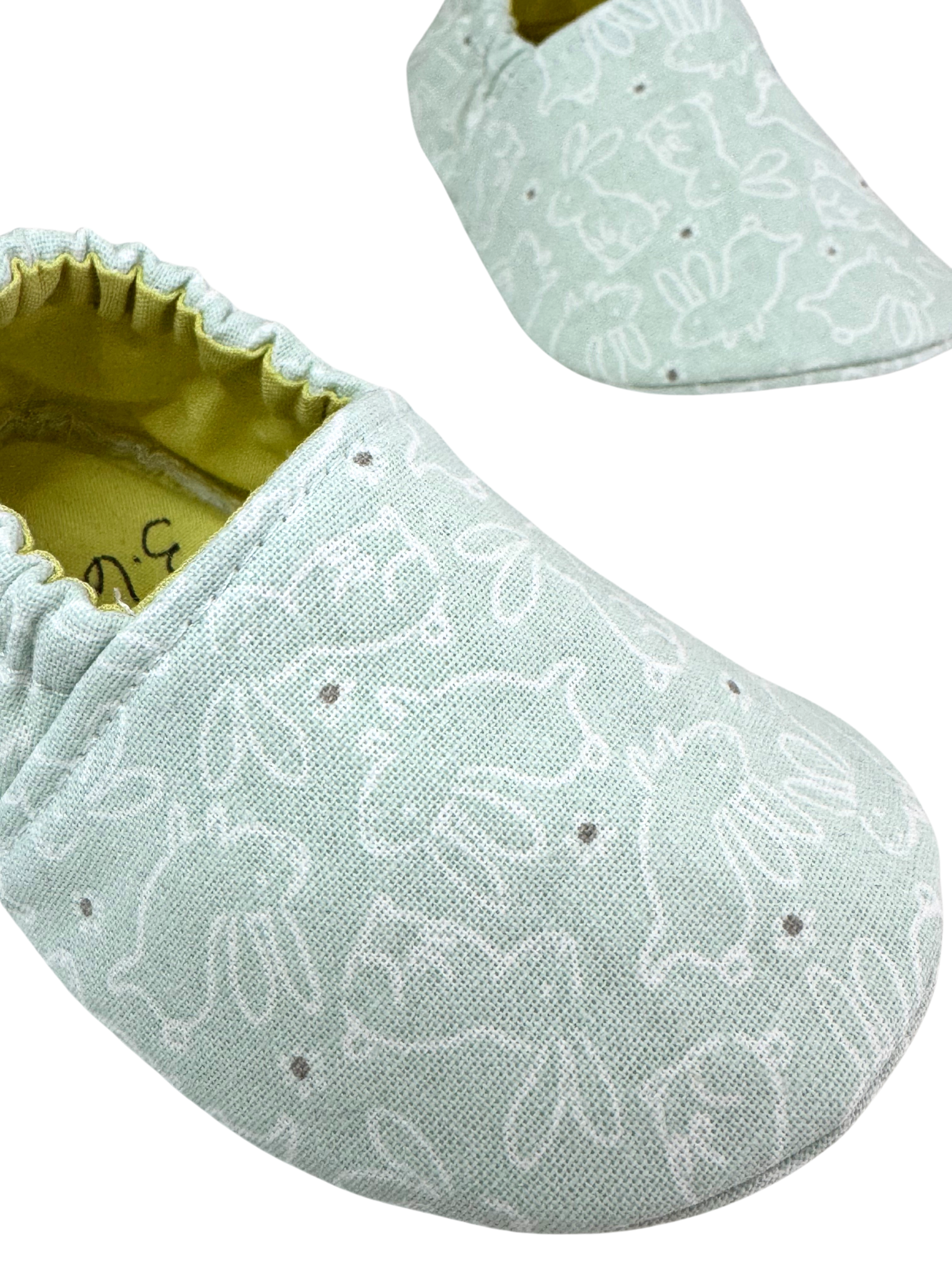 “Close-up of bunny pattern fabric on mint handmade baby shoes with yellow lining, soft sole, 3-6 months”

