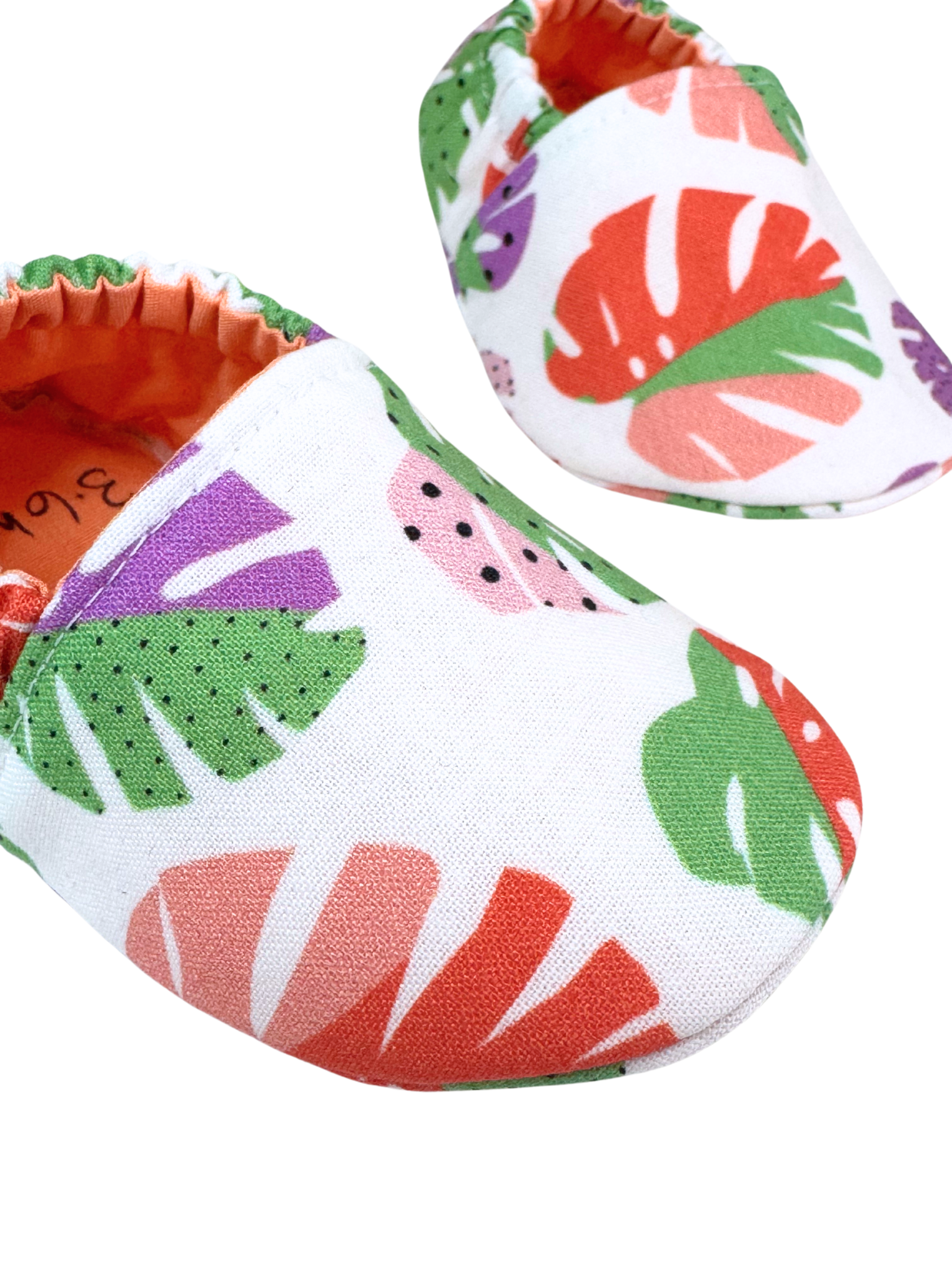 Closeup of monstera print baby shoes with orange lining

