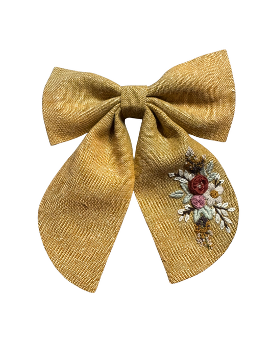Gold bow with floral embroidery on a white background