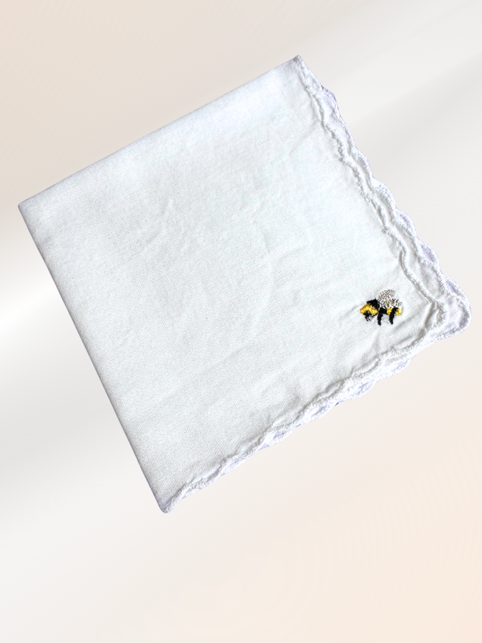 A folded embroidered handkerchief showcasing a delicate bumblebee stitched in fine detail on soft white fabric, handmade in Kansas City.

