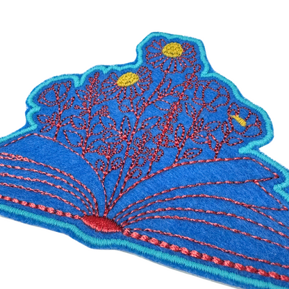 Angled close-up of open book with blooming flowers embroidered patch
