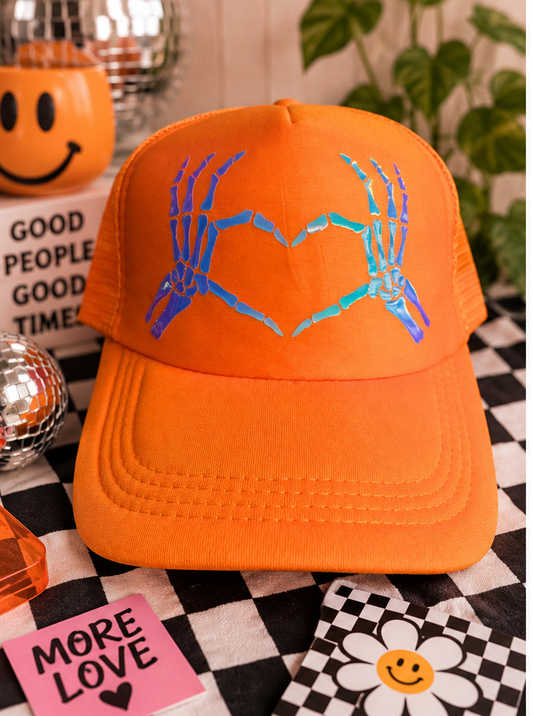 Orange trucker hat with holographic skeleton hands forming a heart, styled product photo