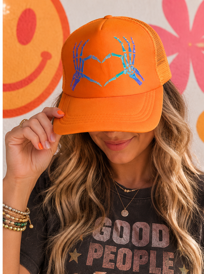 Woman wearing orange skeleton heart hands trucker hat