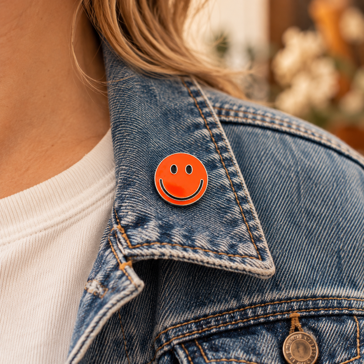 One-inch orange smiley enamel pin worn on a blue denim jacket collar