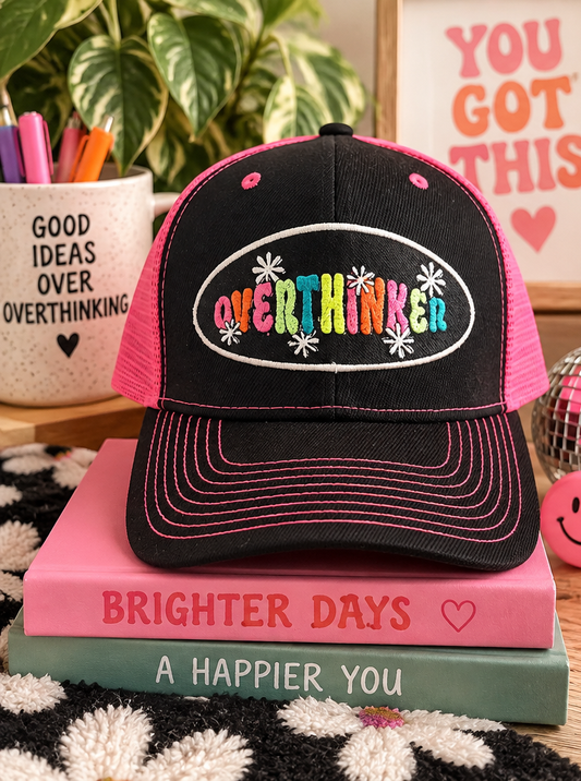 Pink and black Overthinker trucker hat styled with colorful decor