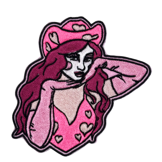 Close-up of an embroidered pink cowgirl patch featuring a heart-studded cowboy hat and flowing hair.
