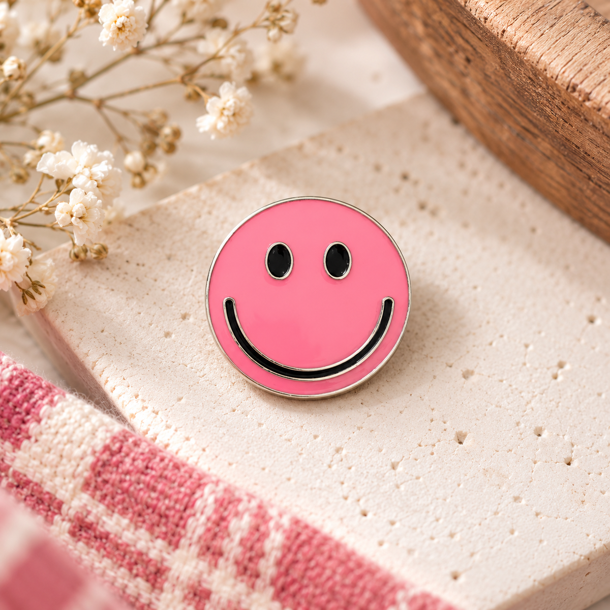 Pink smiley face enamel pin styled on cream stone with flowers