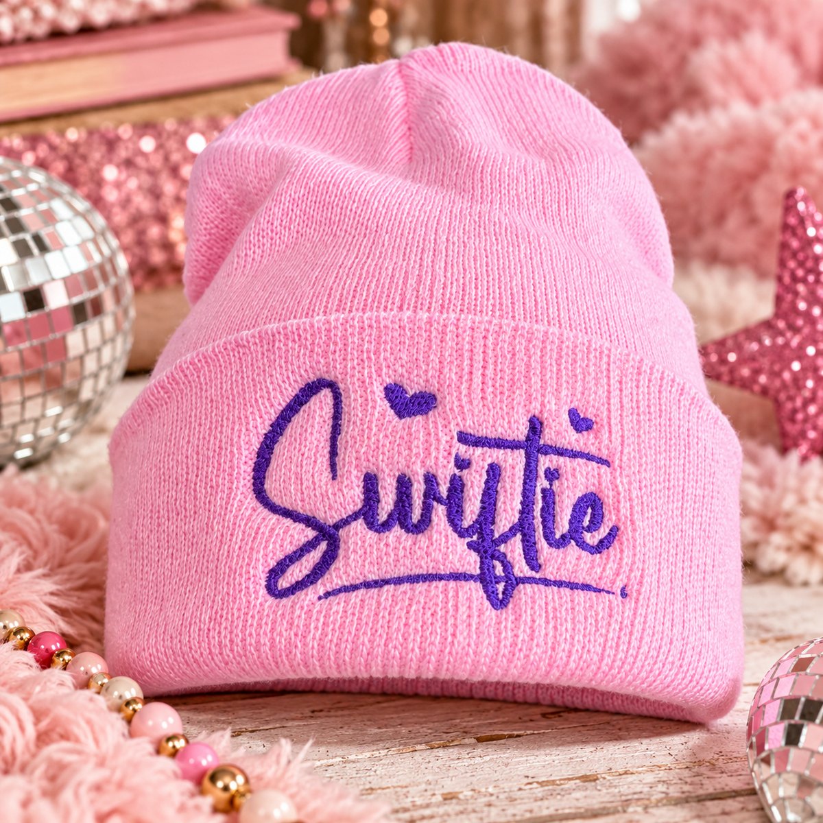 Pink Swiftie embroidered youth beanie with purple script and heart details in a playful pink music-inspired setting.