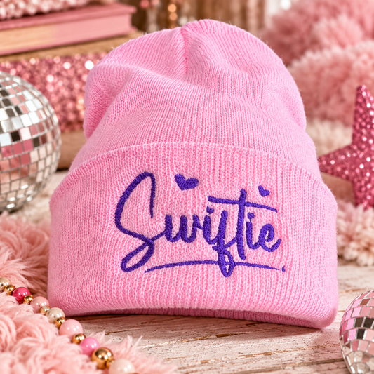 Pink Swiftie embroidered youth beanie with purple script and heart details in a playful pink music-inspired setting.