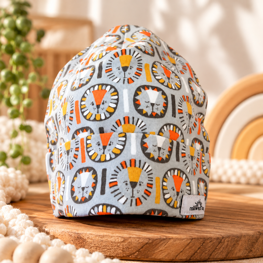Gray organic cotton baby beanie with orange and yellow lion print, styled on wood in a warm nursery
